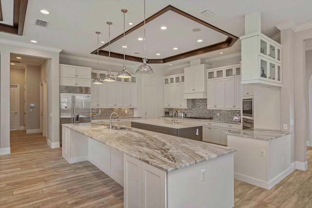 kitchen with a center island with sink, hanging light fixtures, white cabinets, and tasteful backsplash