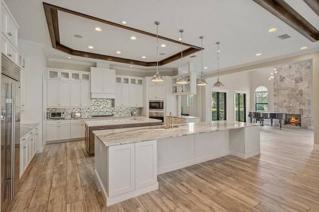 kitchen featuring white cabinets, a large island, a tray ceiling, and light hardwood / wood-style flooring