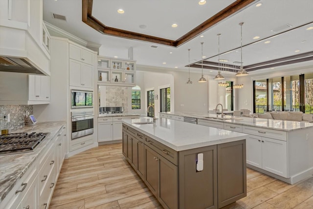 kitchen with a raised ceiling, a center island with sink, tasteful backsplash, and white cabinetry