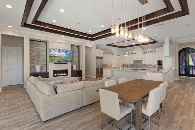 dining area featuring a notable chandelier, ornamental molding, a tray ceiling, and light wood-type flooring