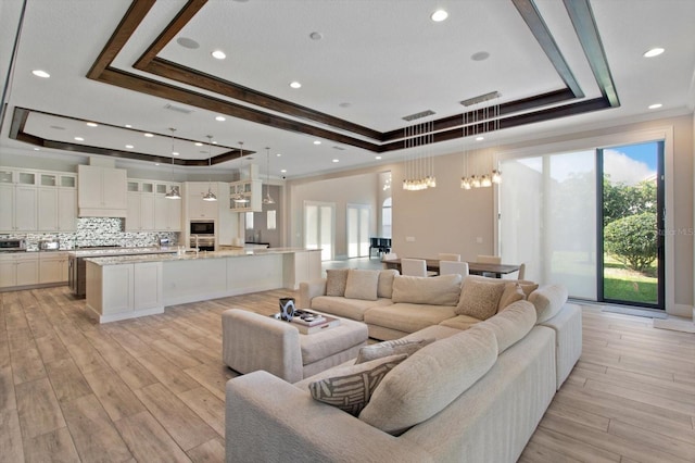 living room featuring a raised ceiling, light hardwood / wood-style floors, crown molding, and a wealth of natural light