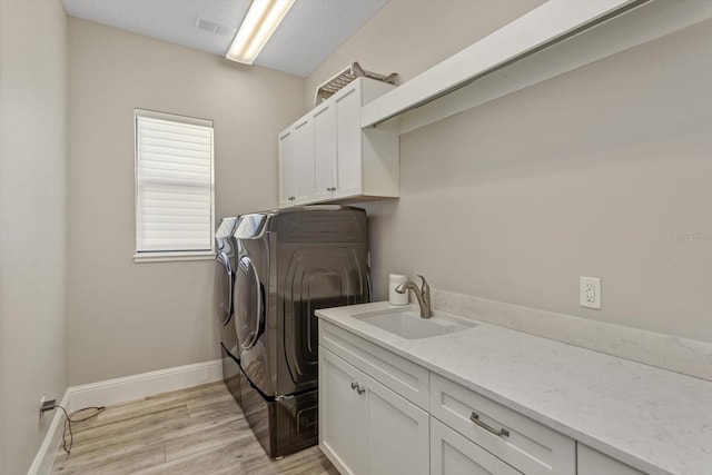 laundry area featuring separate washer and dryer, cabinets, light wood-type flooring, and sink