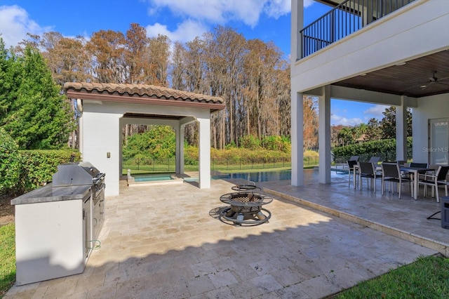 view of patio / terrace with an outdoor fire pit, a swimming pool, grilling area, ceiling fan, and exterior kitchen