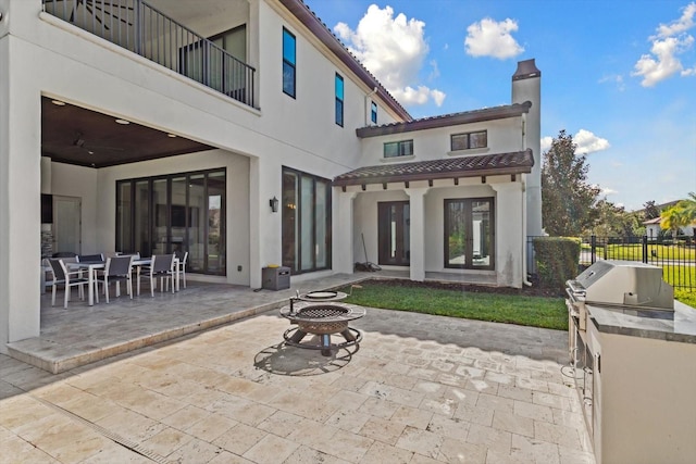 rear view of property featuring ceiling fan, a balcony, a fire pit, a patio, and area for grilling