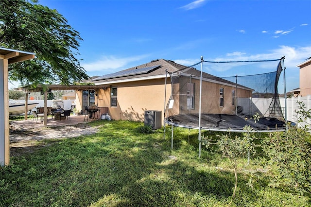 back of house featuring a patio area, a trampoline, solar panels, central AC unit, and a yard