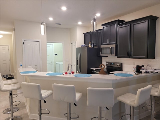 kitchen featuring light tile floors, stainless steel appliances, pendant lighting, and washing machine and dryer