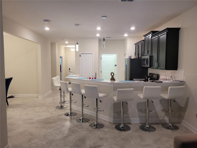 kitchen featuring appliances with stainless steel finishes, tasteful backsplash, light tile floors, hanging light fixtures, and a kitchen breakfast bar