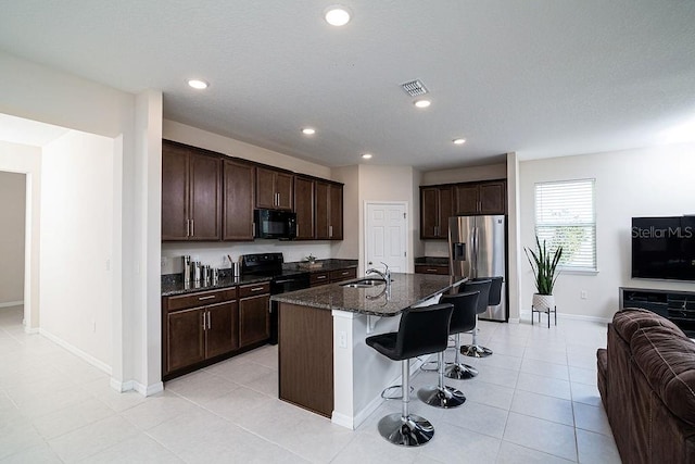 kitchen with a breakfast bar, dark brown cabinets, sink, black appliances, and a center island with sink