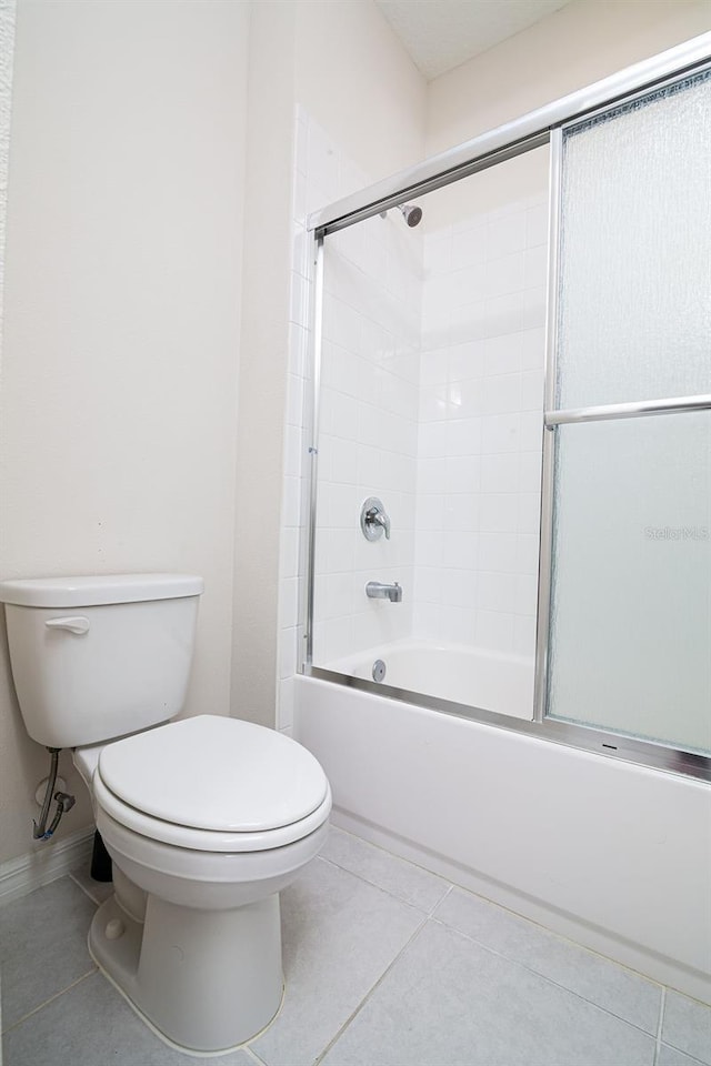 bathroom featuring tile patterned floors, bath / shower combo with glass door, and toilet