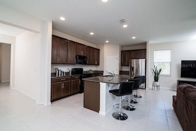 kitchen featuring a center island with sink, a kitchen breakfast bar, electric stove, stainless steel fridge, and dark brown cabinetry