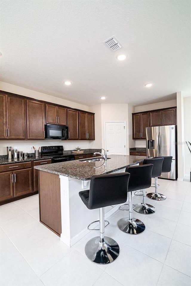 kitchen with sink, dark stone counters, a breakfast bar, black appliances, and a center island with sink