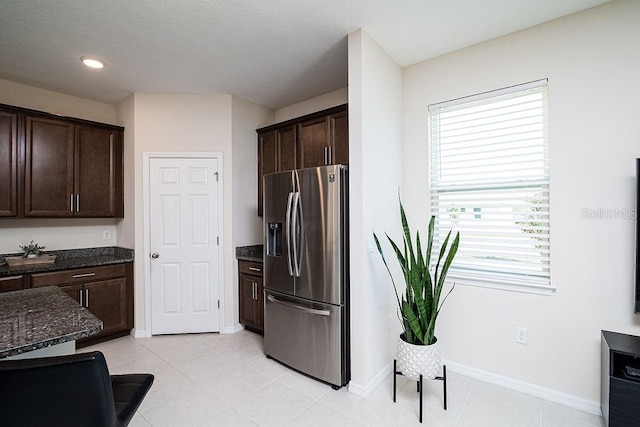 kitchen with dark brown cabinets, dark stone countertops, and stainless steel refrigerator with ice dispenser