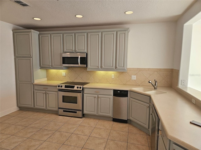 kitchen with light tile floors, backsplash, gray cabinets, and stainless steel appliances