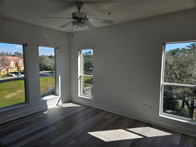 empty room with a healthy amount of sunlight, ceiling fan, and dark wood-type flooring