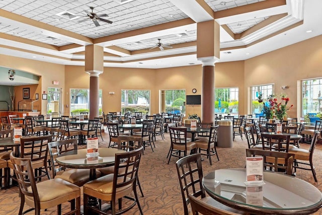 carpeted dining space featuring a high ceiling, a tray ceiling, ornate columns, and ceiling fan