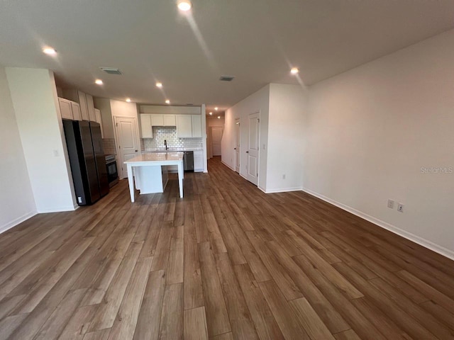 kitchen with black fridge, a kitchen island with sink, hardwood / wood-style floors, and white cabinetry