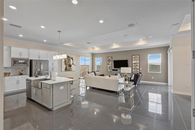 kitchen with white cabinets, a center island with sink, stainless steel appliances, a tray ceiling, and decorative light fixtures