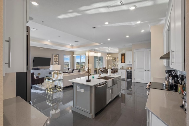 kitchen featuring sink, a center island with sink, stainless steel dishwasher, a raised ceiling, and ornamental molding