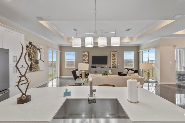 kitchen with pendant lighting, ornamental molding, a center island with sink, a raised ceiling, and tile floors