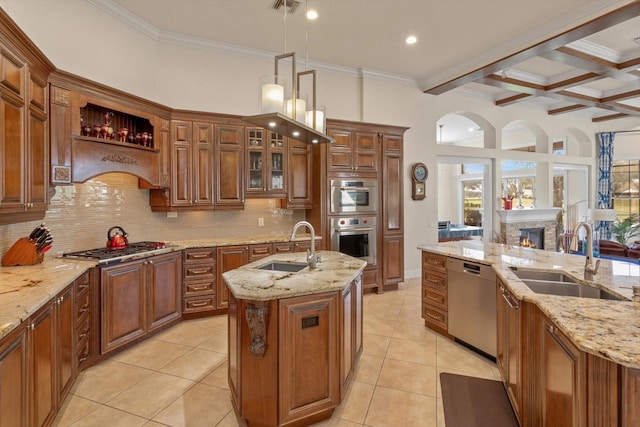 kitchen with decorative light fixtures, a kitchen island with sink, light stone countertops, and stainless steel appliances