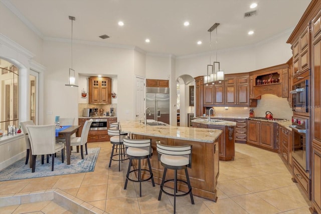 kitchen featuring light tile patterned floors, appliances with stainless steel finishes, a large island with sink, and decorative light fixtures