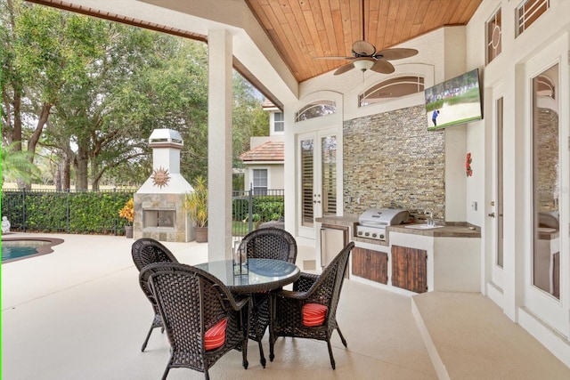 view of patio / terrace with exterior kitchen, ceiling fan, an outdoor stone fireplace, and area for grilling