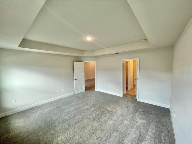 empty room featuring a tray ceiling and dark colored carpet