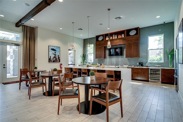 dining space with beamed ceiling, beverage cooler, and light wood-type flooring