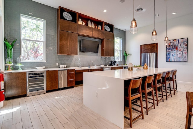 kitchen with wine cooler, stainless steel appliances, decorative light fixtures, a kitchen island, and backsplash