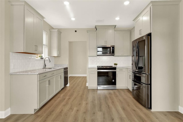 kitchen featuring appliances with stainless steel finishes, sink, tasteful backsplash, and light hardwood / wood-style flooring