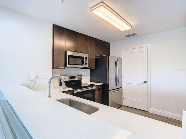 kitchen featuring appliances with stainless steel finishes, dark brown cabinets, sink, and light wood-type flooring