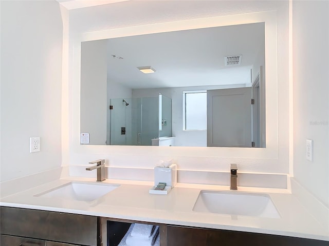 bathroom featuring toilet, dual vanity, and a shower with shower door