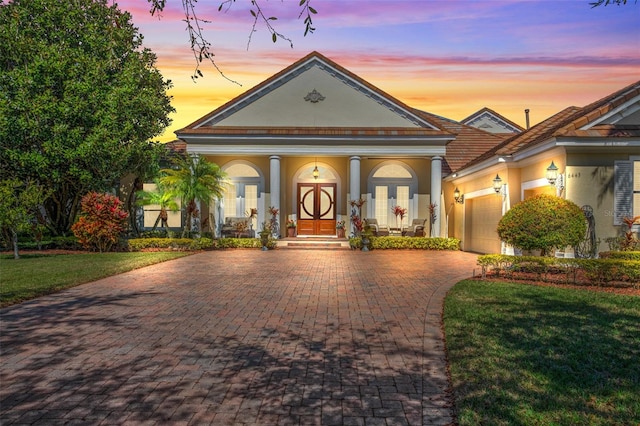 neoclassical / greek revival house featuring an attached garage, french doors, decorative driveway, stucco siding, and a front yard