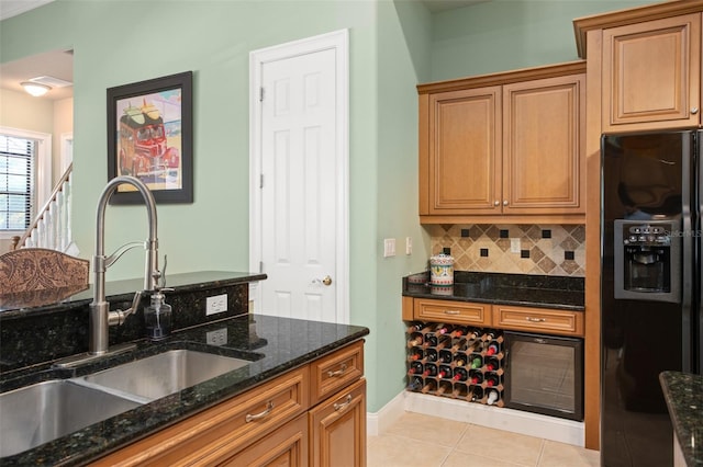 kitchen featuring light tile patterned floors, dark stone counters, black fridge with ice dispenser, a sink, and backsplash