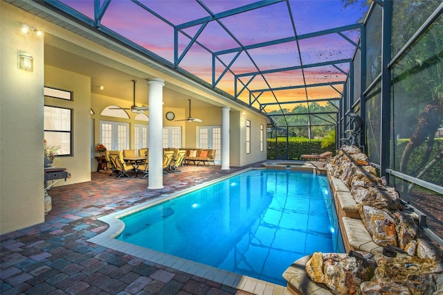 pool at dusk with a pool with connected hot tub, outdoor dining space, a patio area, ceiling fan, and a lanai