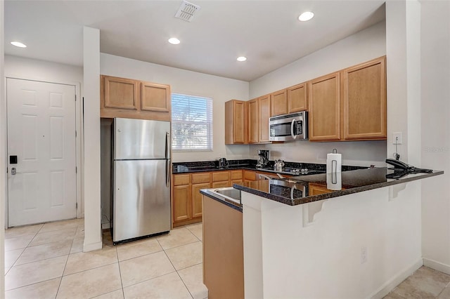 kitchen with light tile flooring, stainless steel appliances, kitchen peninsula, and dark stone counters