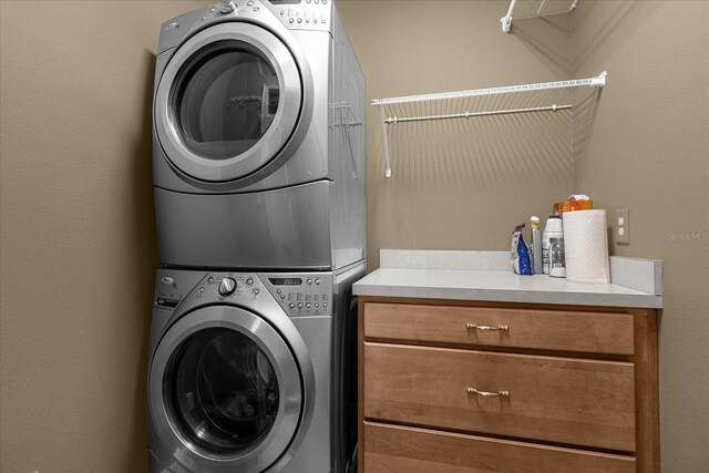 laundry area featuring stacked washing maching and dryer and cabinets