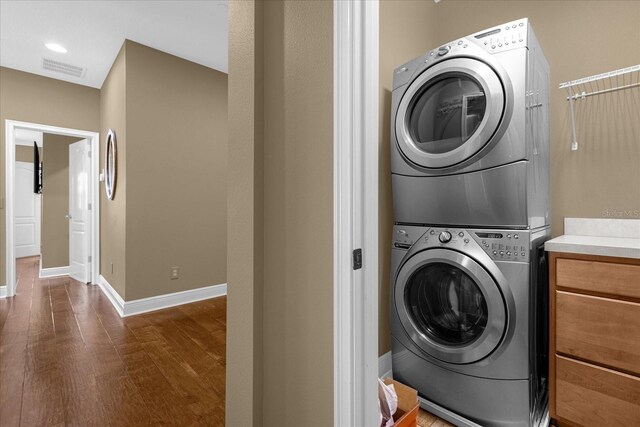 clothes washing area with stacked washer / drying machine and dark wood-type flooring