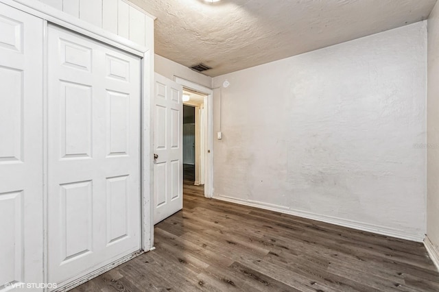 unfurnished bedroom featuring a textured ceiling, dark hardwood / wood-style flooring, and a closet