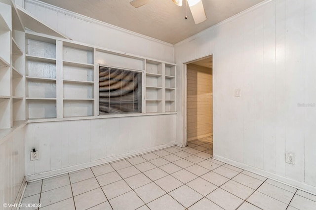 unfurnished room with wooden walls, built in shelves, ceiling fan, ornamental molding, and light tile patterned flooring