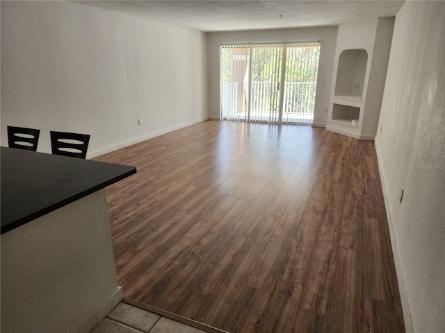 unfurnished living room featuring built in features, a textured ceiling, and wood-type flooring