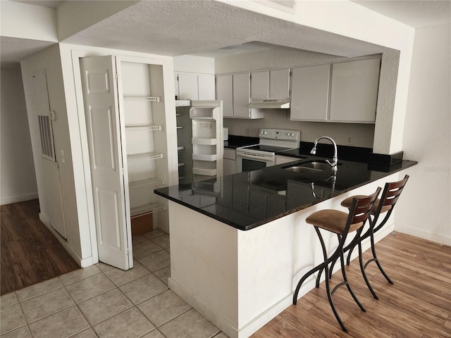 kitchen featuring kitchen peninsula, light tile flooring, sink, and electric range