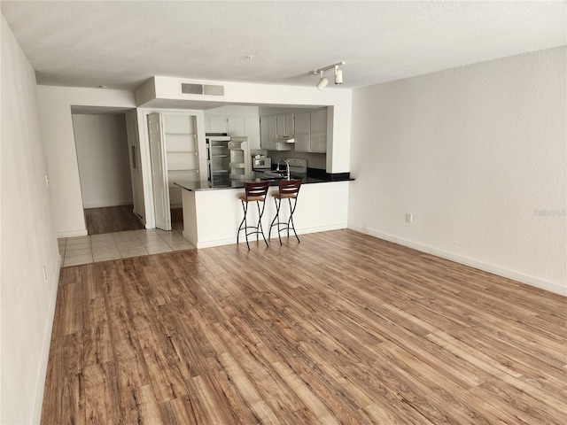 kitchen featuring light tile floors, kitchen peninsula, a breakfast bar area, gray cabinetry, and track lighting