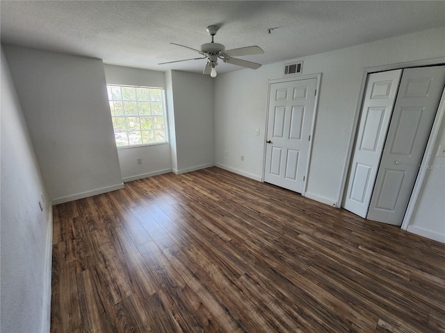 unfurnished bedroom with two closets, ceiling fan, a textured ceiling, and dark hardwood / wood-style flooring