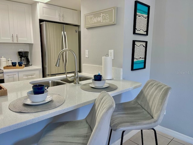 kitchen featuring light stone countertops, white cabinetry, stainless steel fridge, light tile flooring, and a kitchen breakfast bar