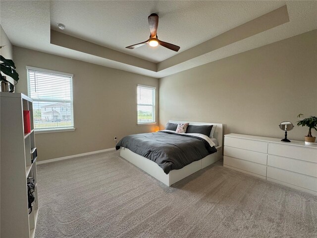 bedroom with a tray ceiling, ceiling fan, and light carpet