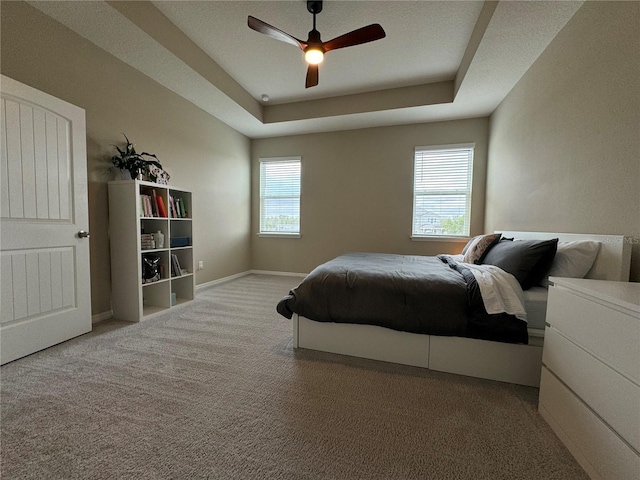 carpeted bedroom with a raised ceiling and ceiling fan