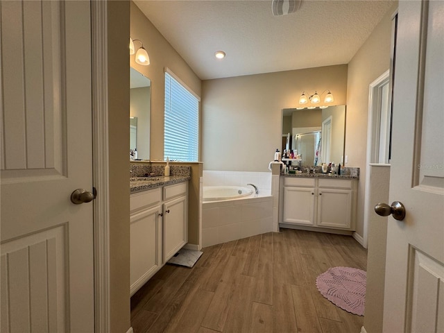 bathroom featuring tiled tub, vanity, a textured ceiling, and hardwood / wood-style flooring