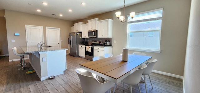 kitchen featuring appliances with stainless steel finishes, a center island with sink, white cabinets, light hardwood / wood-style floors, and hanging light fixtures