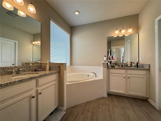 bathroom with tiled bath, vanity, a textured ceiling, and hardwood / wood-style flooring